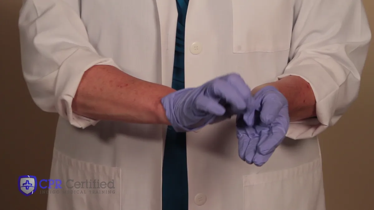 A gloved hand pinching the outside of the other glove near the wrist, starting to peel it back.