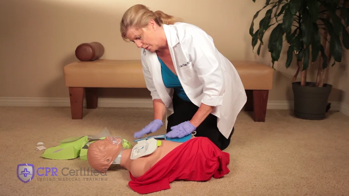 Both AED pads on a bare chest with the machine beside it, and the rescuer sitting back with hands off.